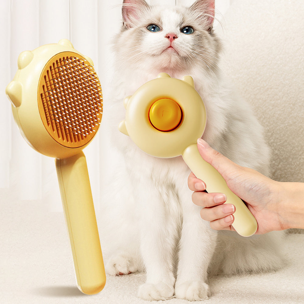 Yellow pet grooming brush with metal bristles for cats and dogs held near a fluffy white cat with blue eyes