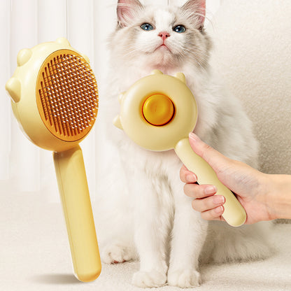 Yellow pet grooming brush with metal bristles for cats and dogs held near a fluffy white cat with blue eyes