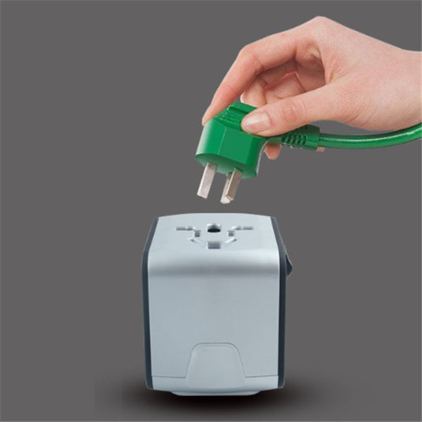Hand holding green plug above gray universal travel adapter with multiple socket types on gray background