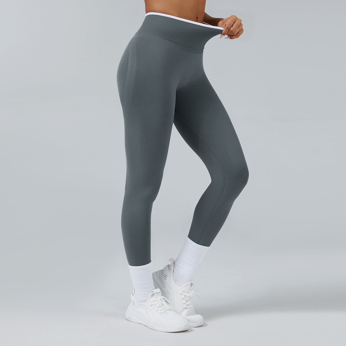 Woman wearing high-waist seamless gray workout leggings with white sneakers and socks on gray background