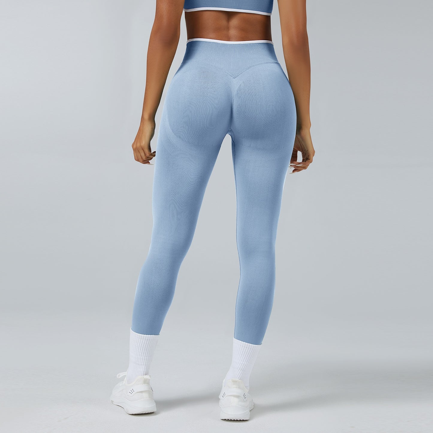 Back view of woman wearing seamless light blue high-waist workout leggings and white sneakers on gray background
