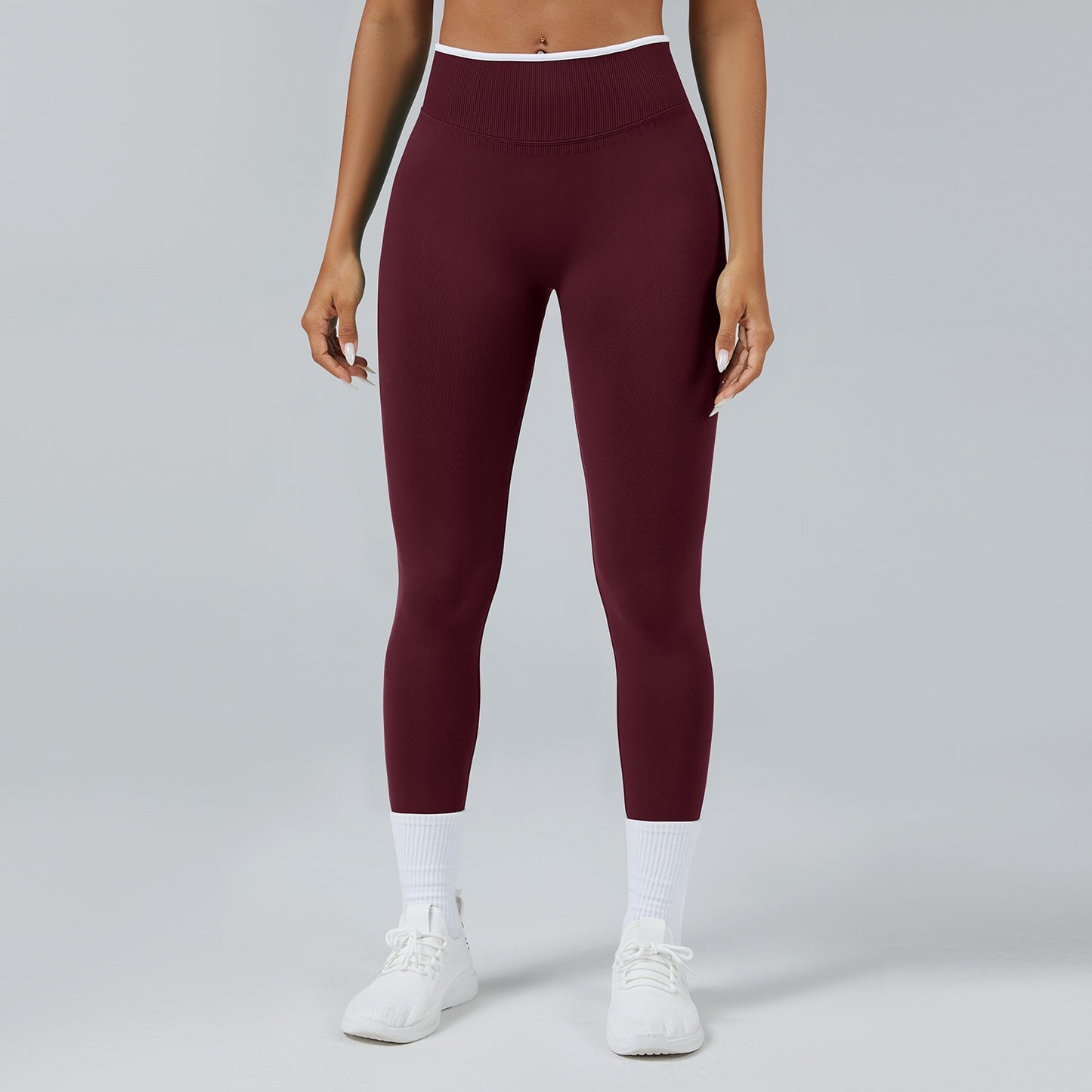 Woman wearing high-waist seamless maroon leggings with white sneakers and socks on gray background
