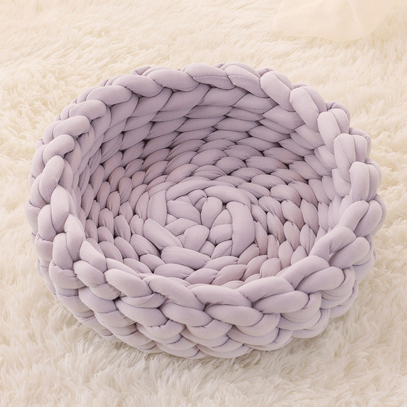 Grey round plush cat bed with braided soft cushion on fluffy white surface
