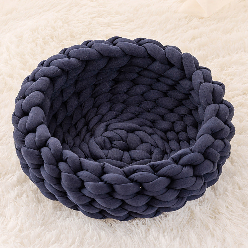 Dark grey knitted round plush cat bed on a white fluffy surface