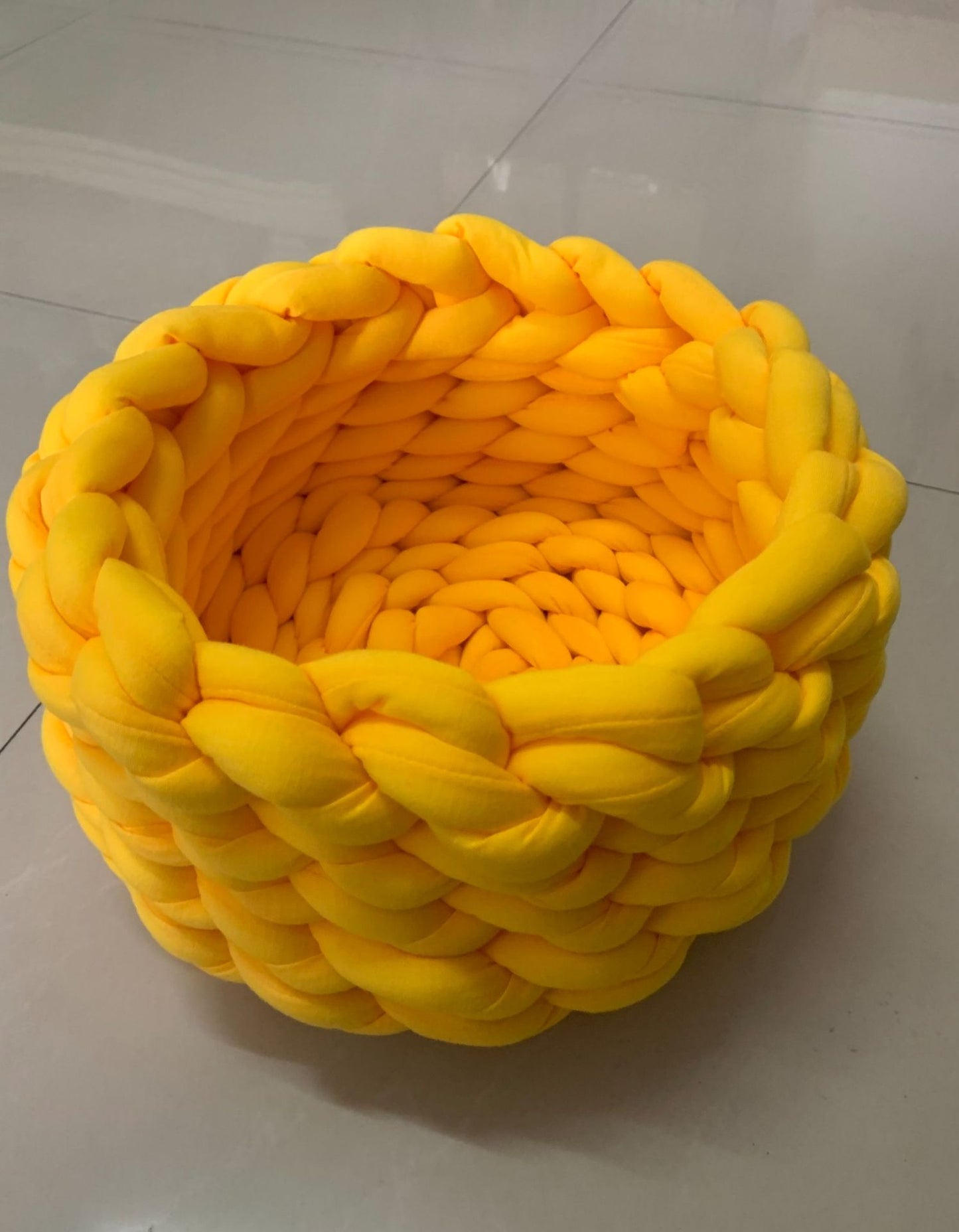 Round yellow plush knitted pet bed on light tile floor