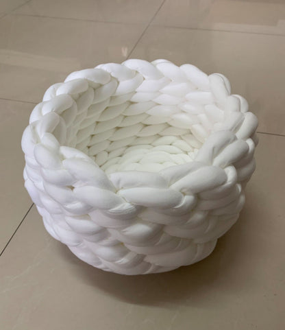 Round white plush cat bed with thick braided edges on beige floor