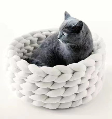 Grey cat sitting in a soft, round, white braided plush cat bed on a white background