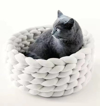 Grey cat sitting in a soft, round, white braided plush cat bed on a white background