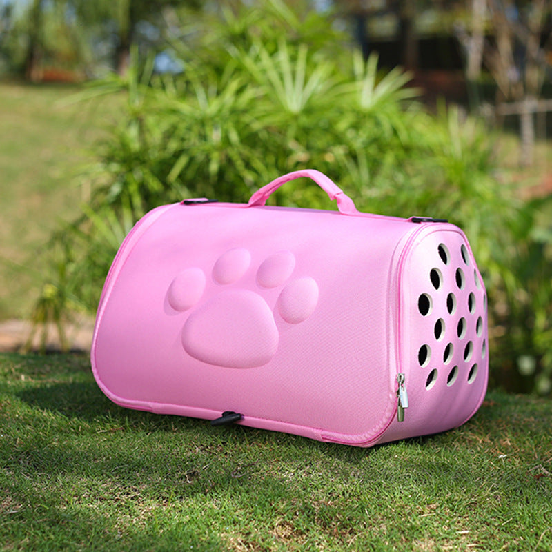 Pink foldable pet carrier with paw print design and ventilation holes on grass outdoors
