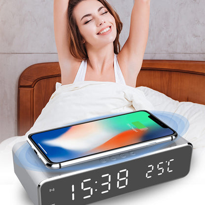 Grey LED digital alarm clock with wireless phone charger and temperature display on bedside table