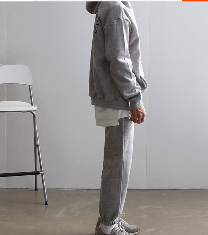 Side view of a man wearing grey hooded sweatshirt and matching sweatpants with athletic sneakers indoors