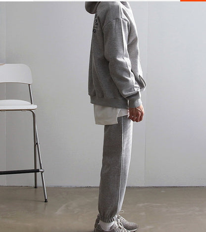 Side view of a man wearing grey hooded sweatshirt and matching sweatpants with athletic sneakers indoors