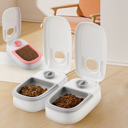 Three automatic pet feeders with open lids, filled with dry food, on a wooden floor with a chair in background