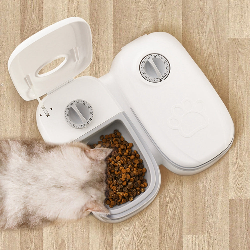 Automatic white pet feeder with timer and dry food bowl on wooden floor, cat eating