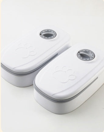 Two white automatic pet feeders with paw print design and timer dials on top