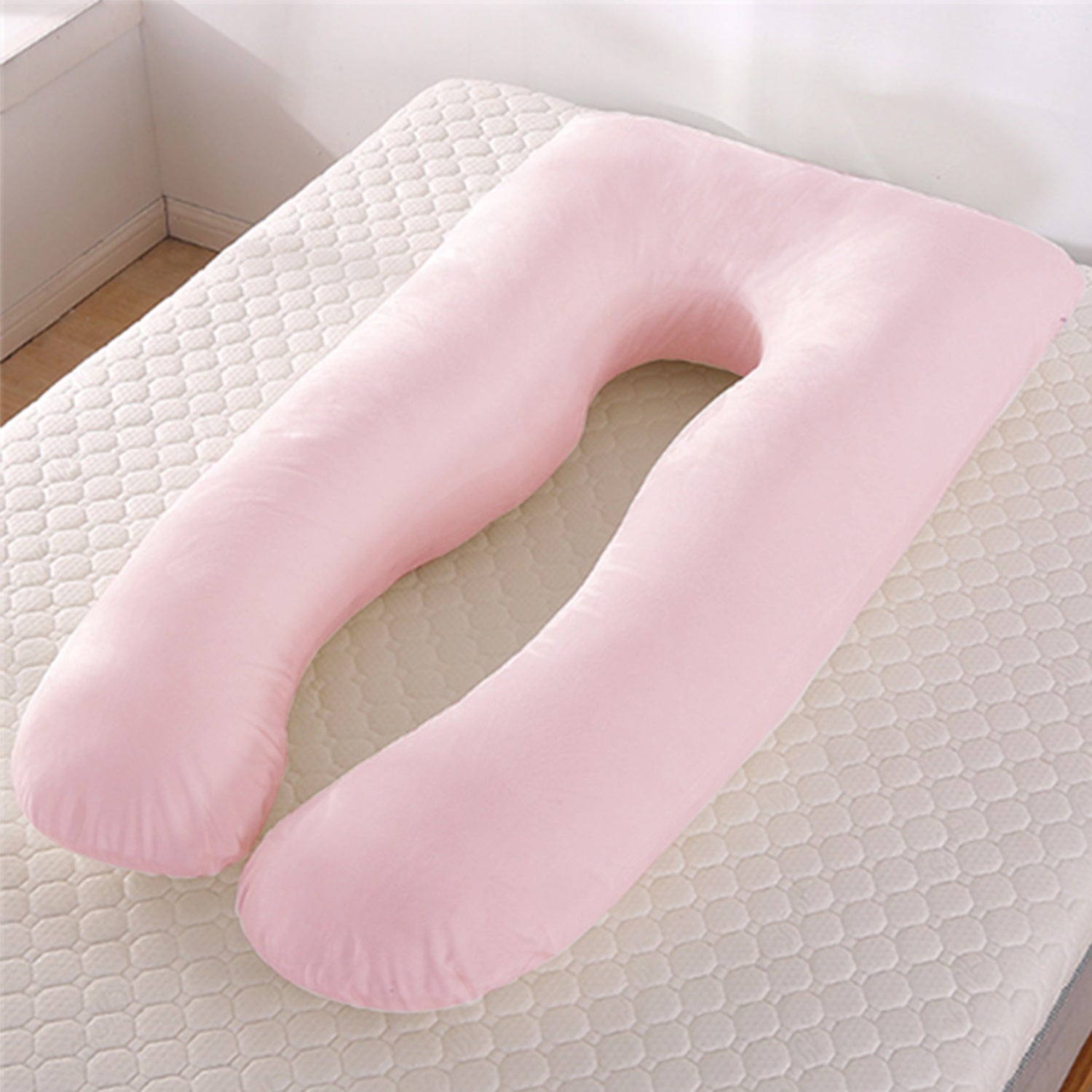 Soft pink U-shaped maternity pillow on a beige mattress with hexagonal pattern