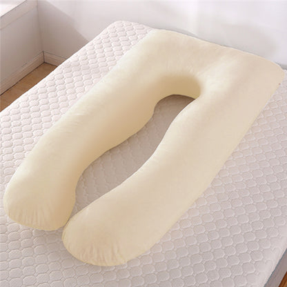 Beige U-shape maternity pillow on a white quilted mattress in a bright room