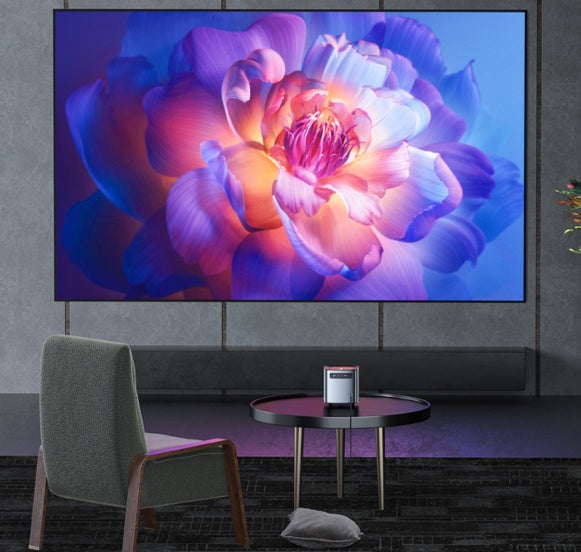 Mini portable projector on black round table displaying vibrant flower image on wall in modern living room