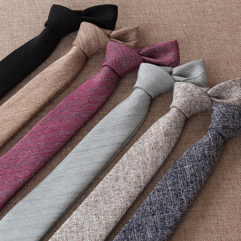 Six slim cotton ties in black, beige, pink, light gray, tan, and navy laid on brown fabric