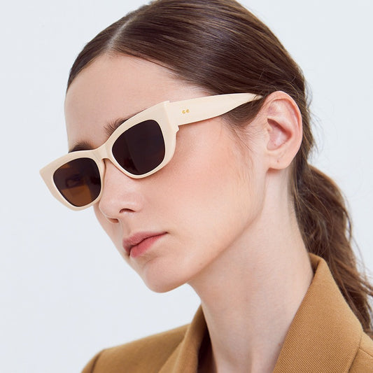 Close-up of woman wearing beige rectangular sunglasses with brown lenses and brown blazer against white background