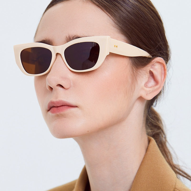 Close-up of woman wearing cream-colored rectangular sunglasses with dark lenses and brown blazer
