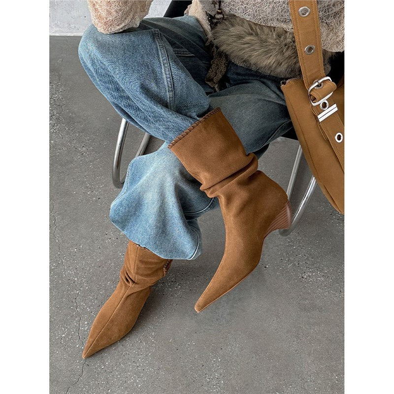 Brown suede pointed toe western boots with low heel worn with blue denim jeans on concrete floor