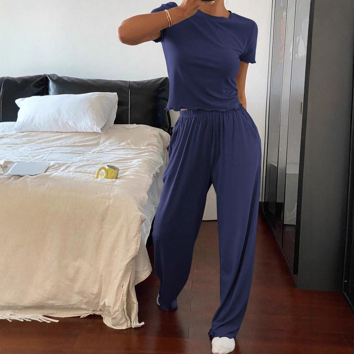 Woman in navy blue casual loungewear set posing in modern bedroom with bed and mug