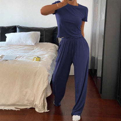 Woman in navy blue casual loungewear set posing in modern bedroom with bed and mug
