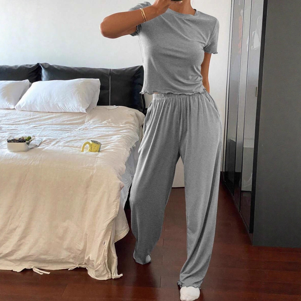 Woman in grey soft cotton casual loungewear set posing in modern bedroom with white bed and wooden floor
