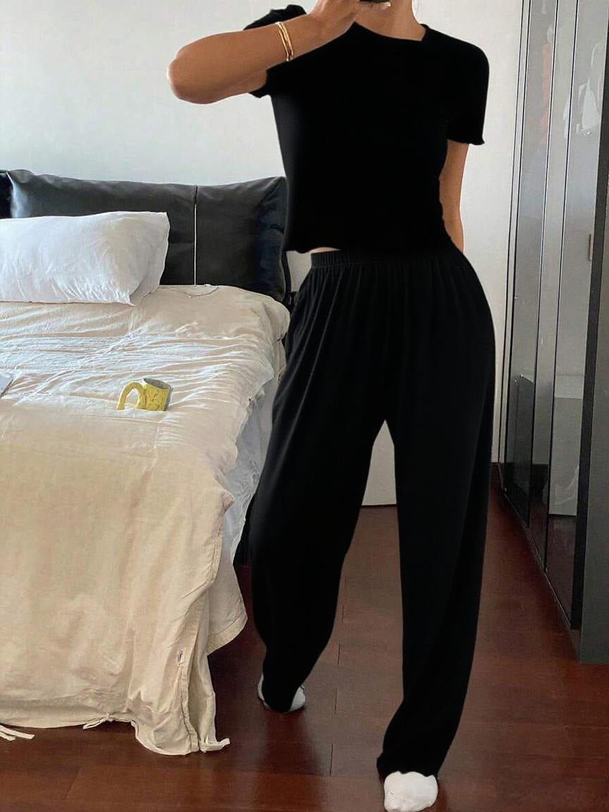 Woman in black casual outfit posing in modern bedroom with bed and wooden floor