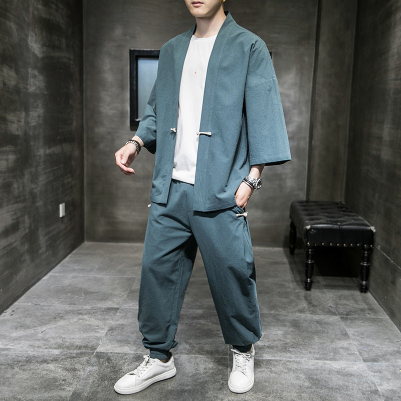 Man wearing loose-fit blue linen Hanfu suit with white sneakers in gray minimalist room