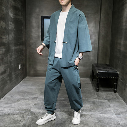 Man wearing loose-fit blue linen Hanfu suit with white sneakers in gray minimalist room