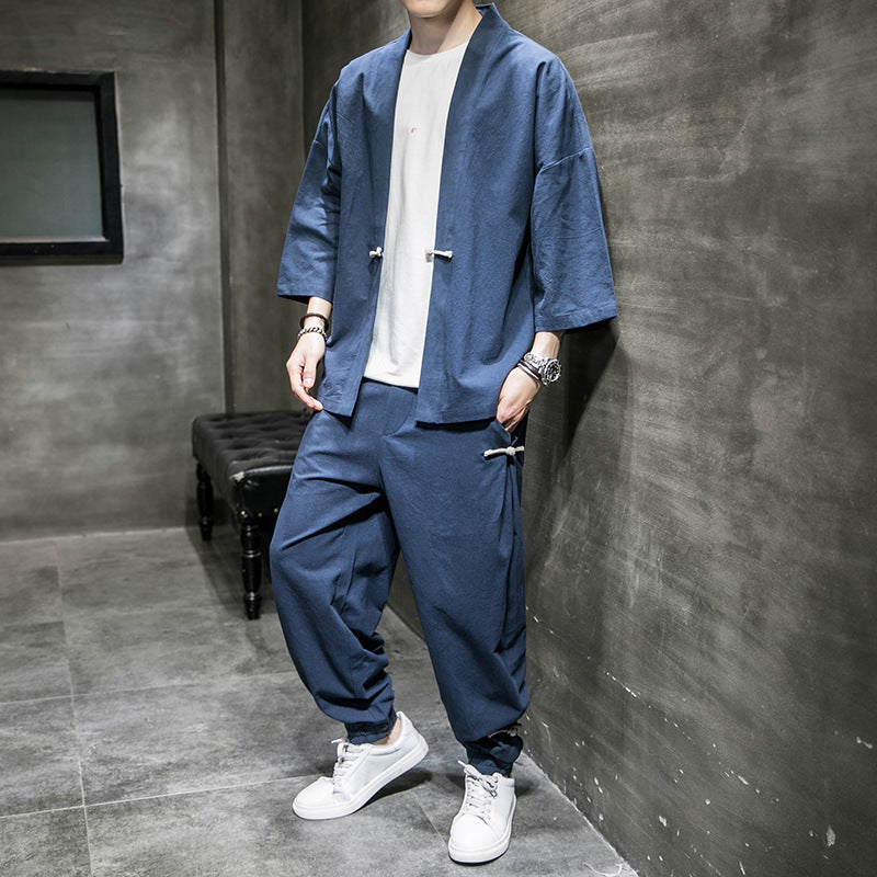 Man wearing loose-fit navy blue linen Hanfu suit with white sneakers, standing in modern grey room