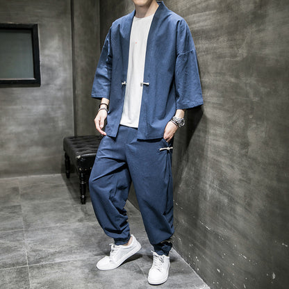 Man wearing loose-fit navy blue linen Hanfu suit with white sneakers, standing in modern grey room