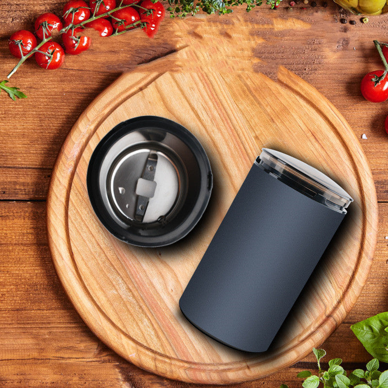 Navy blue electric herb grinder on wooden round cutting board with cherry tomatoes and herbs