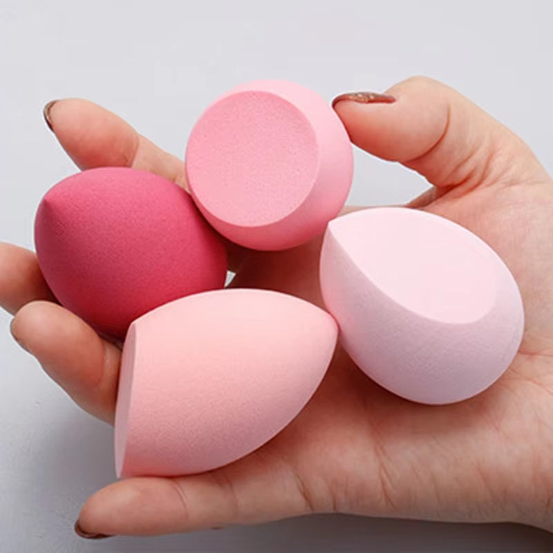 Hand holding four soft makeup blending sponges in various pink shades and shapes