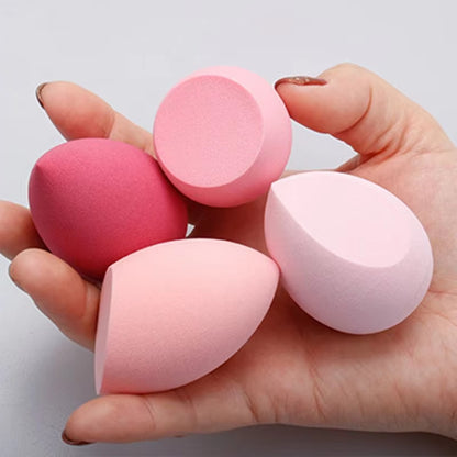 Hand holding four soft makeup blending sponges in various pink shades and shapes