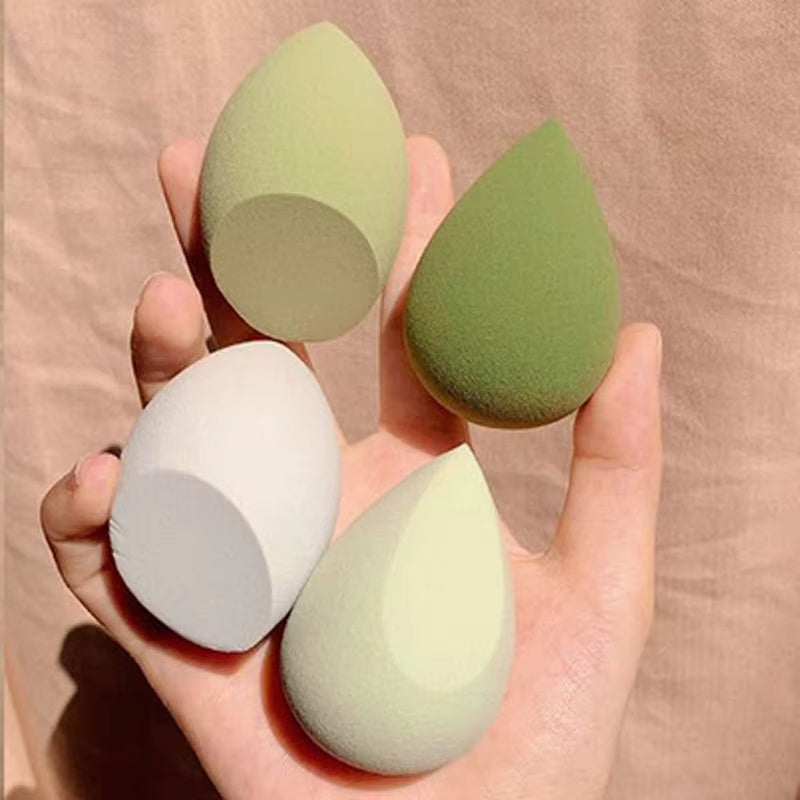 Hand holding four soft makeup sponge blenders in neutral tones on beige background