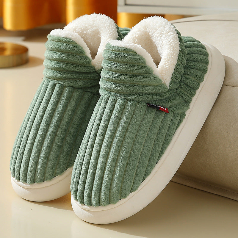 Green ribbed plush slippers with white fleece lining and white soles on a beige surface