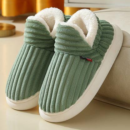 Green ribbed plush slippers with white fleece lining and white soles on a beige surface