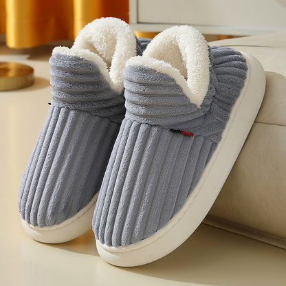 Gray plush indoor slippers with white fleece lining and white soles on a beige surface
