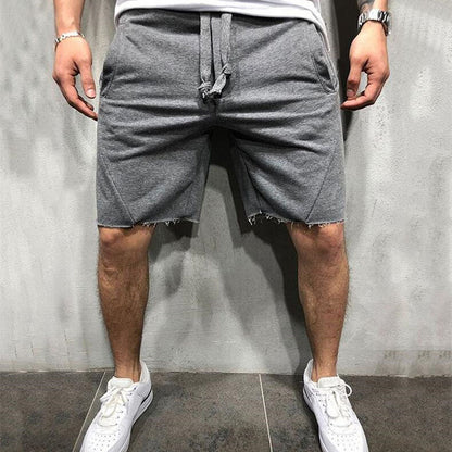 Man wearing grey cotton gym shorts with raw hem and drawstring, paired with white sneakers