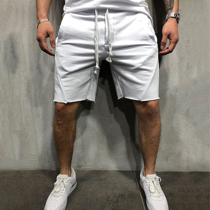 Man wearing white casual cotton gym shorts with drawstring and white sneakers standing against grey wall