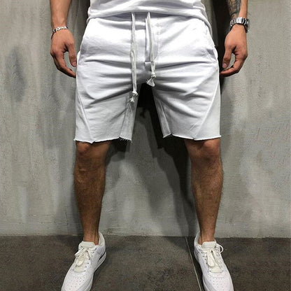 Man wearing white casual cotton gym shorts with drawstring and white sneakers standing against grey wall