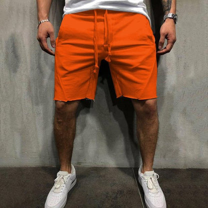 Man wearing bright orange cotton gym shorts with drawstring and a white t-shirt against a gray wall