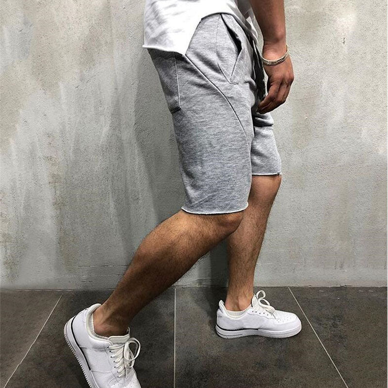 Man wearing breathable grey cotton gym shorts and white athletic sneakers standing on dark tiled floor