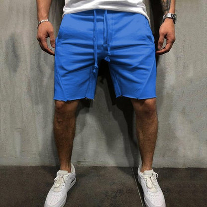 Man wearing bright blue cotton drawstring shorts and white sneakers against a grey wall