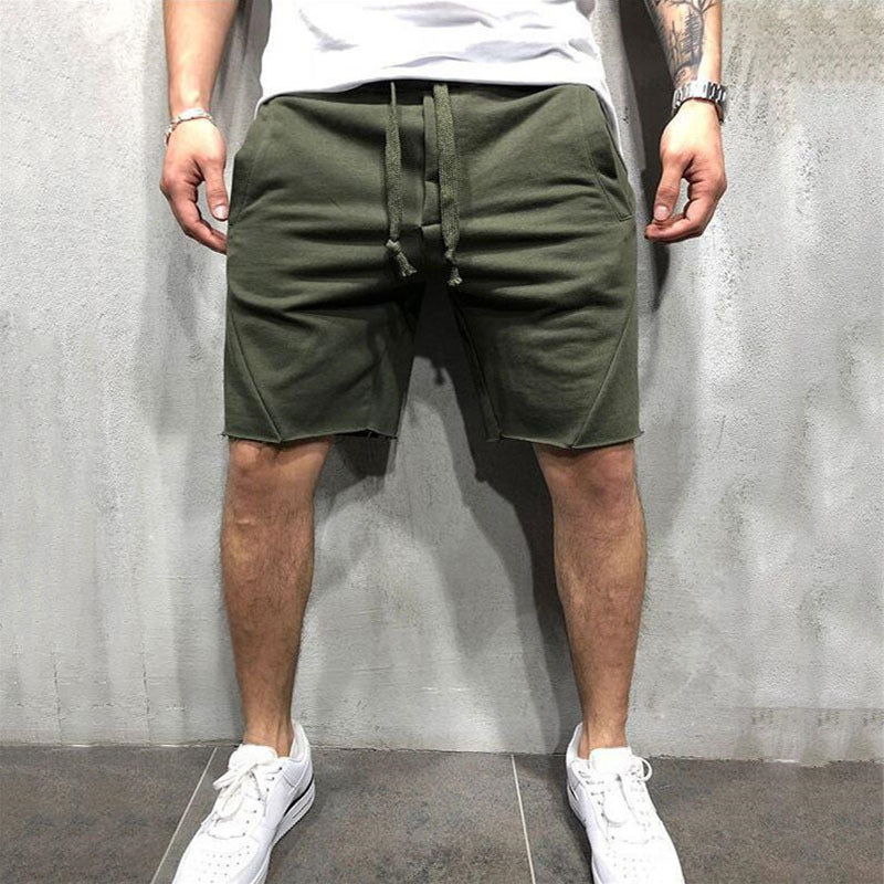 Man wearing olive green cotton gym shorts with drawstring standing against gray wall