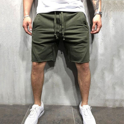 Man wearing olive green cotton gym shorts with drawstring standing against gray wall