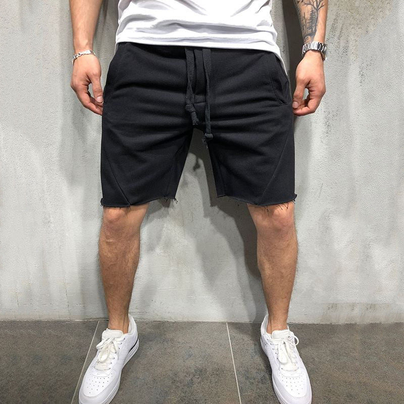 Man wearing black drawstring casual shorts and white sneakers against gray textured wall